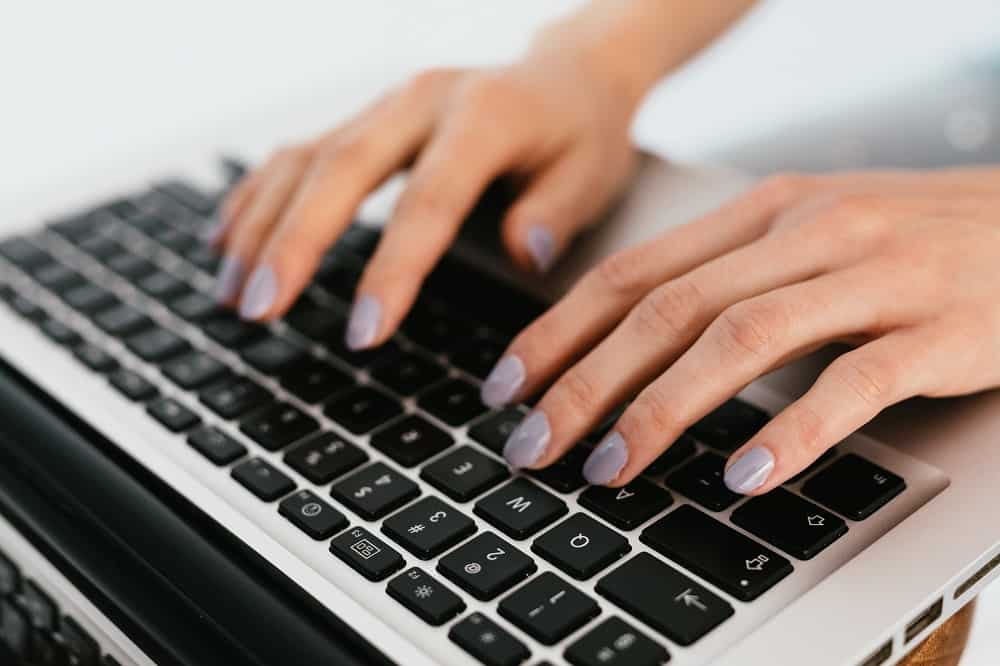 Woman with a light purple manicure typing on a macbook laptop