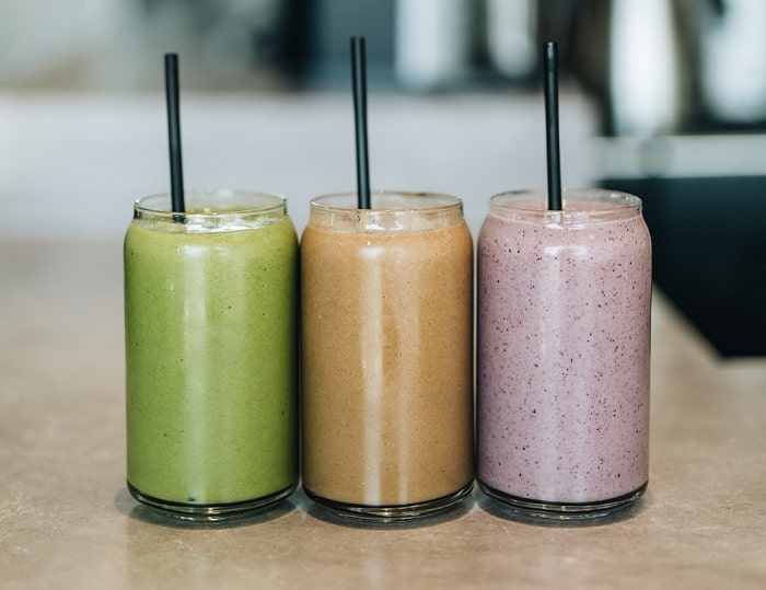 Three bright smoothies in clear glasses lined up on a tabletop 