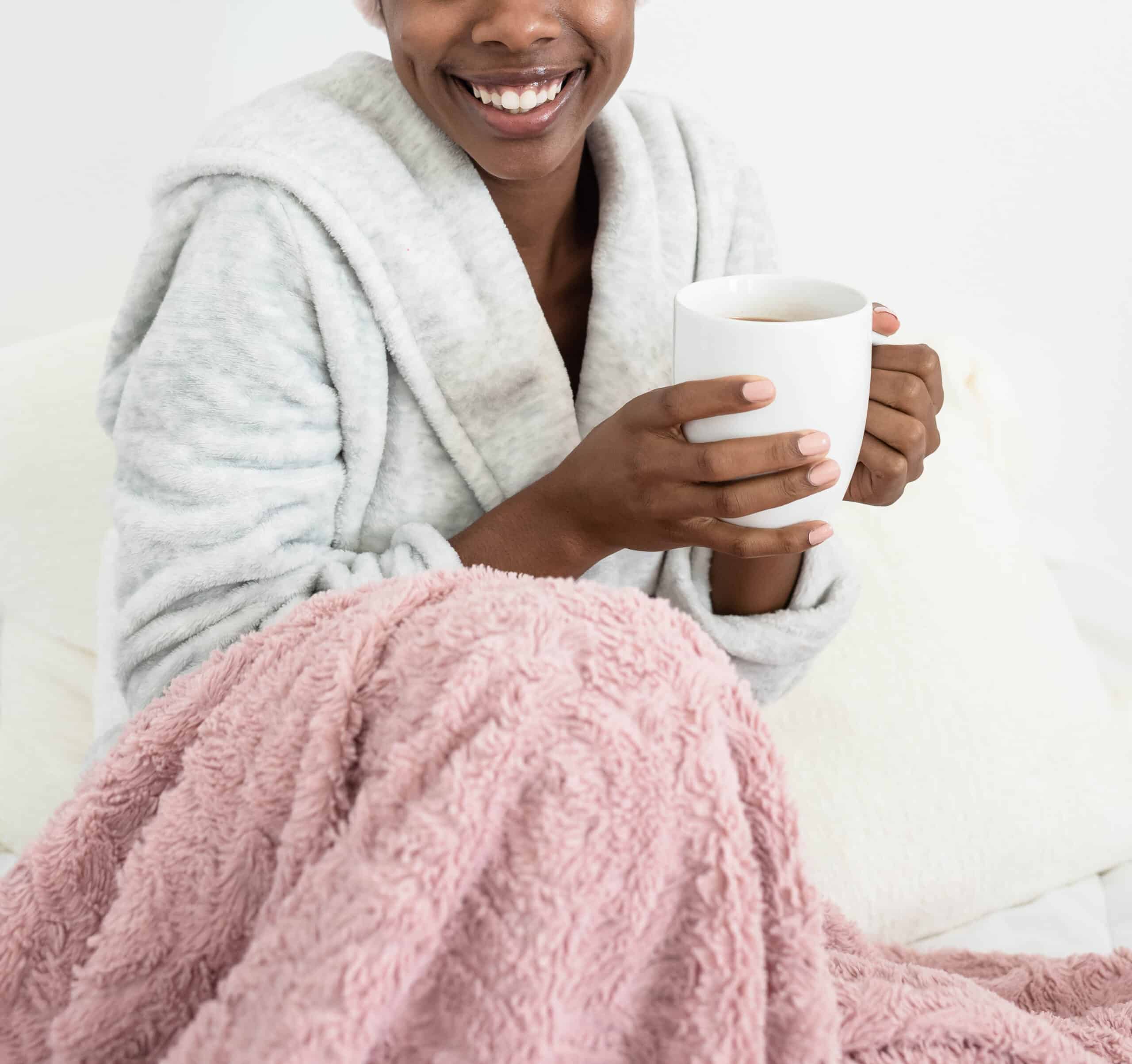 Woman smiling with a mug in her hands and a blanket on her lap
